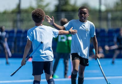 Two primary boys high fiveing whilst playing hockey